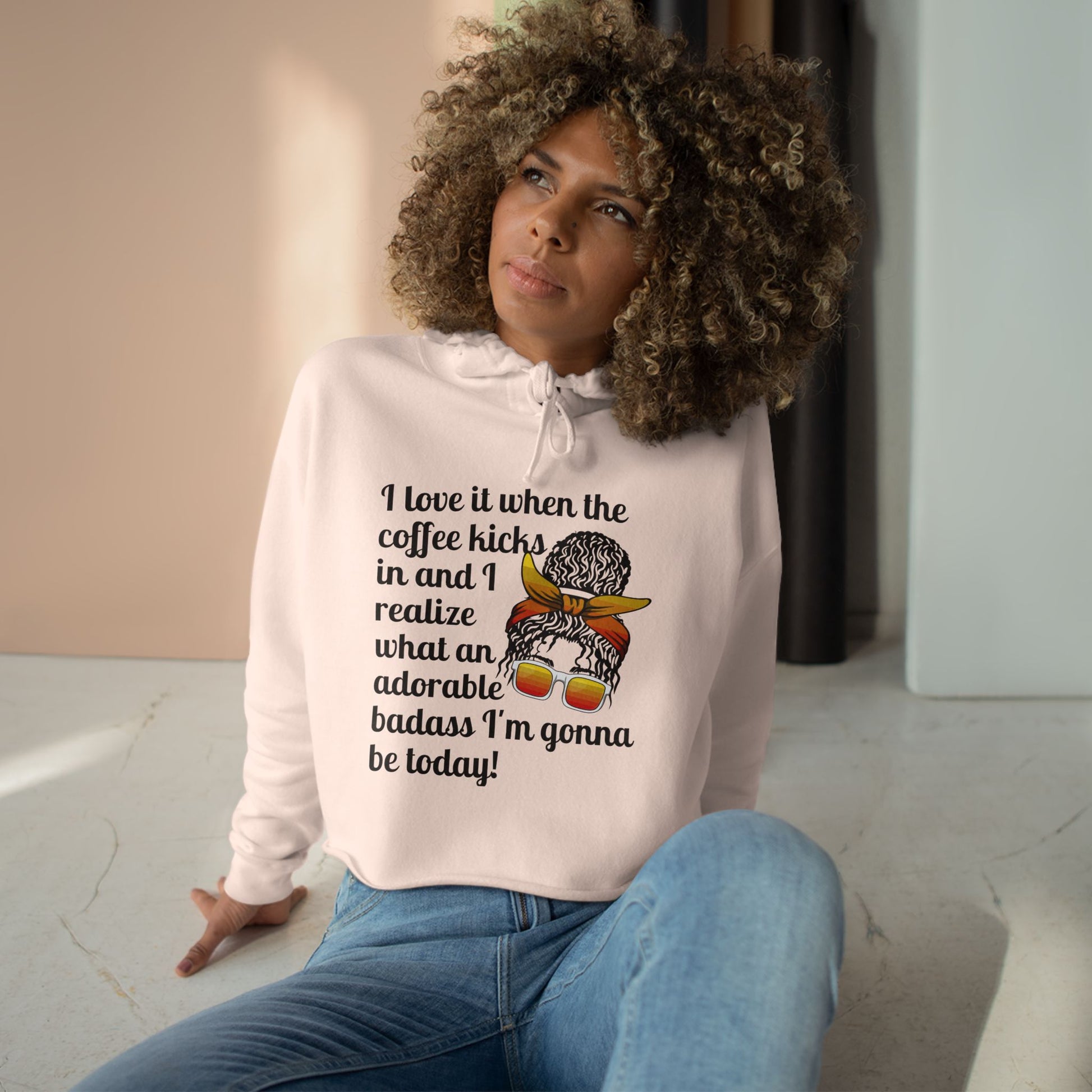 A stylish cropped hoodie printed with "I love it when the coffee kicks in and I realize what an adorable bad ass I'm gonna be today!" with a curly messy bun woman with orange glasses and knotted head band - coral