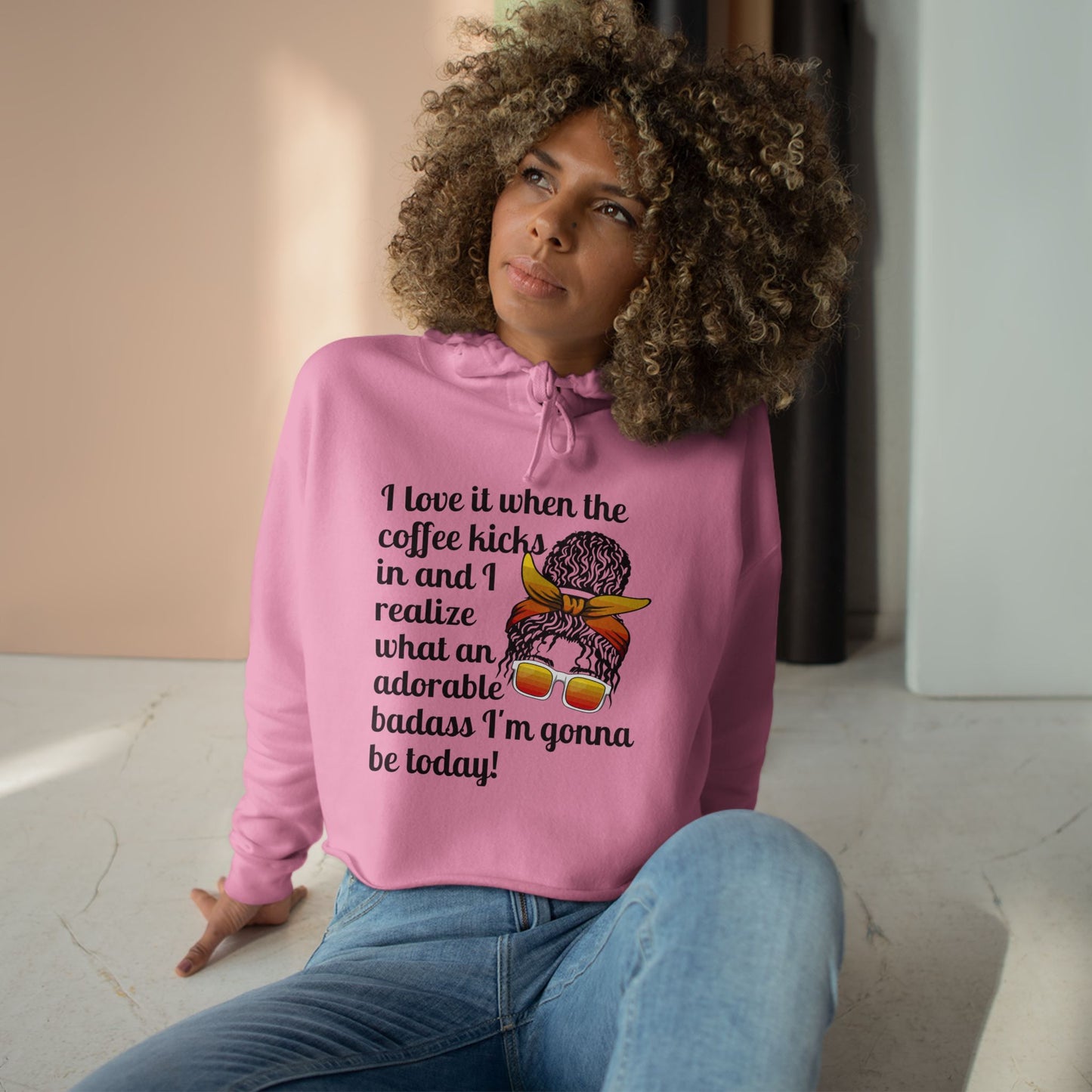 A stylish cropped hoodie printed with "I love it when the coffee kicks in and I realize what an adorable bad ass I'm gonna be today!" with a curly messy bun woman with orange glasses and knotted head band - pink