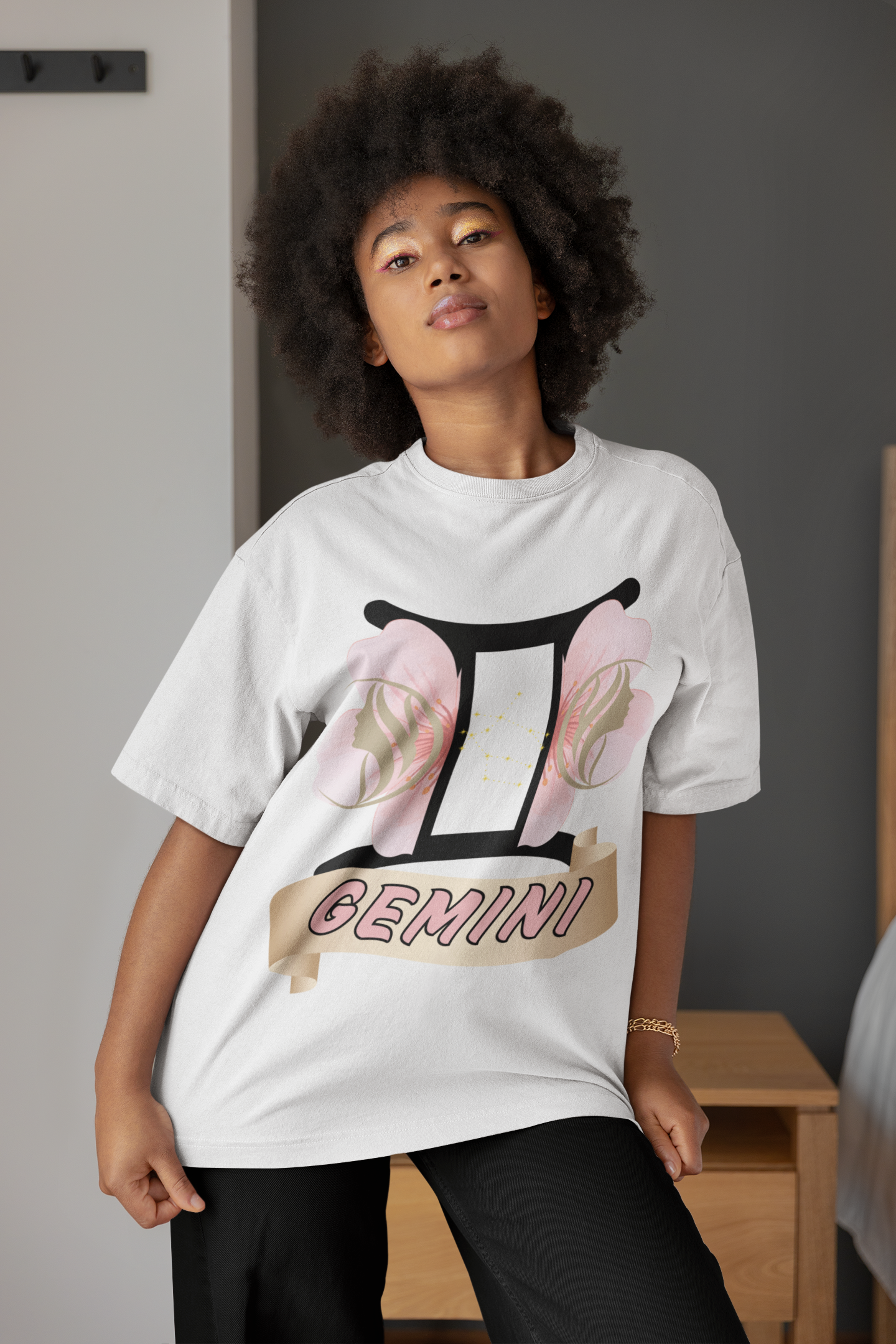 Large black Gemini symbol with a split cherry blossom on each side of the symbol. Gold female side profiles facing away from each other on top of the cherry blossom representing the Gemini. Gemini written in bold light pink font outlined in gold - printed on a white shirt