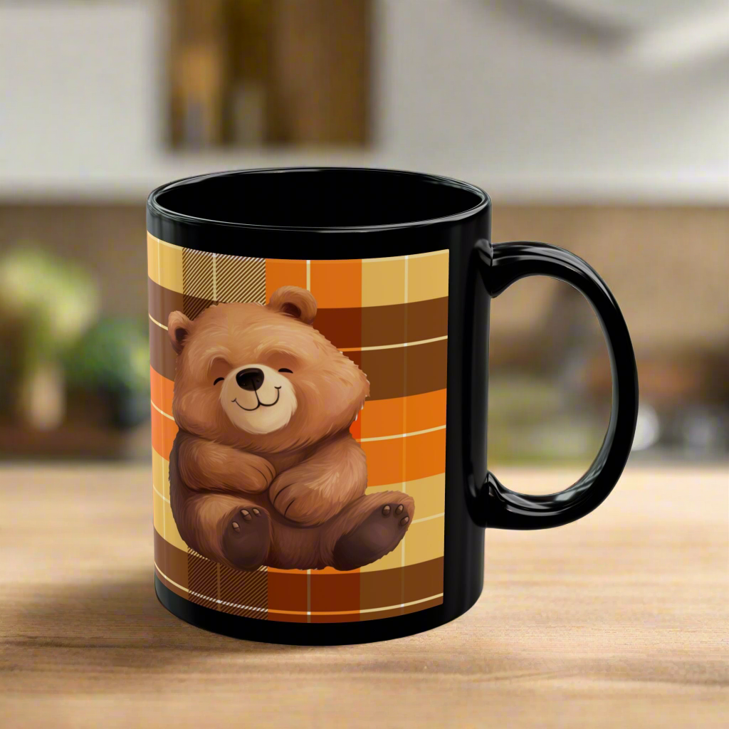 Black Mug with an orange and brown plaid design. I Heart Hoodie Season printed with a white heart next to an adorable teddy bear