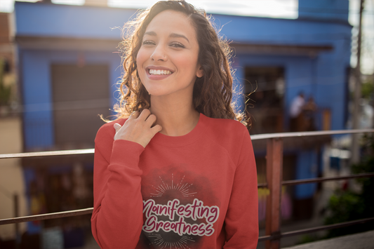 This crewneck sweatshirt is a mix between retro and inspirational. Manifesting Greatness is printed in Retro font in a deep red color with a light grey outline. It has a deep smokey background and small spark lines above and underneath. - Red Crewneck