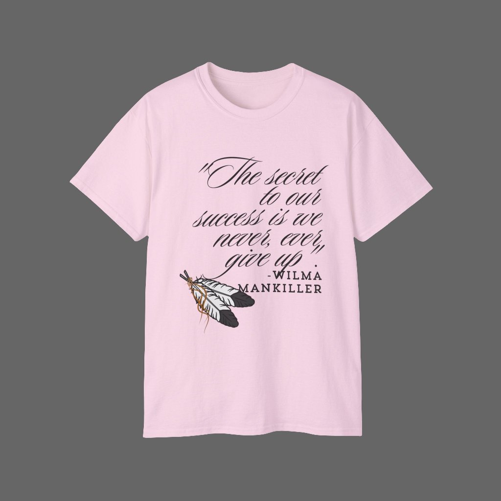 Native American Success Tshirt - Light pink shirt quoting Wilma Mankiller stating the secret to our success is that we never ever give up. Eagle feathers in the corner tied together with leather string. 