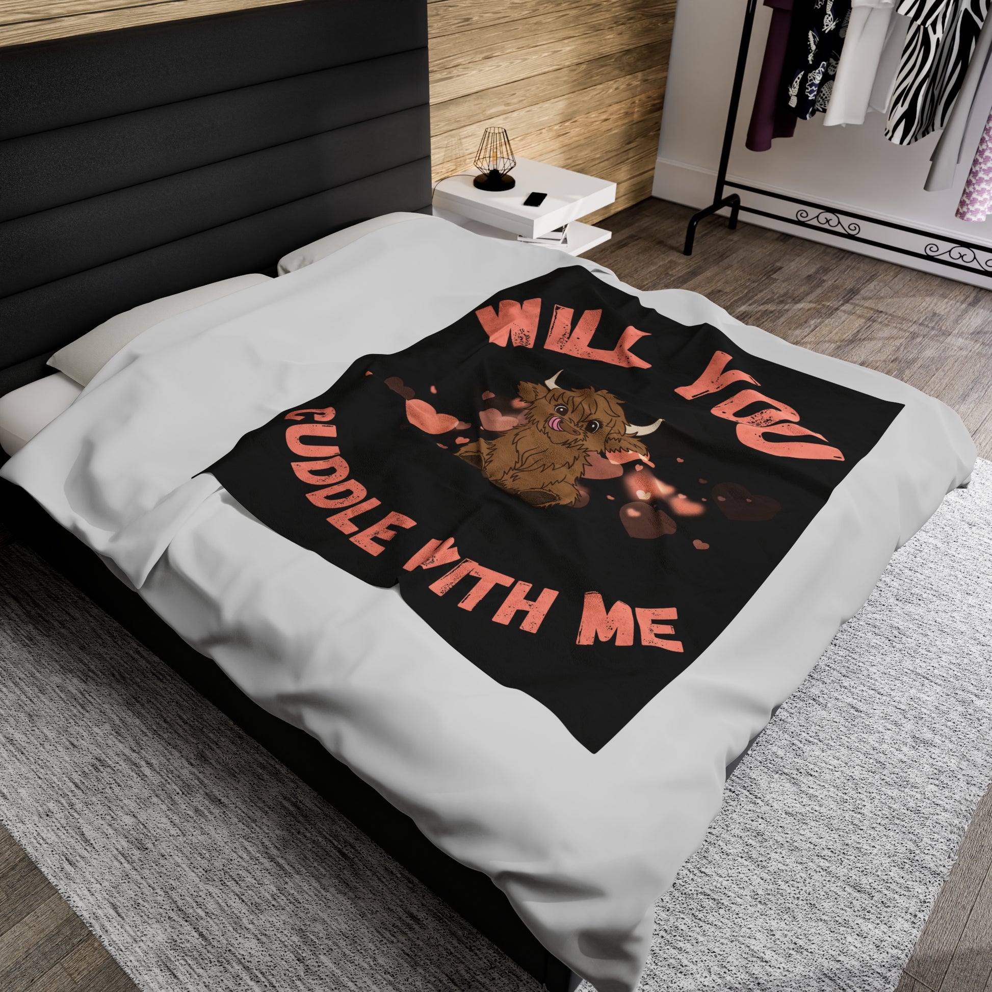 An adorable Scottish Highland Cow in the center of a black blanket with a background of pink hearts. Will you cuddle with me is printed around the cow in large pink font. Perfect as a gift for that special lady in your life